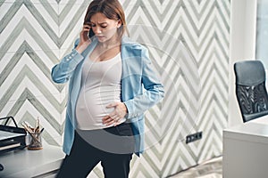 Upset pregnant woman talking on cellphone in office