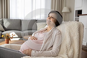 Charming expectant mother relax in comfy chair at living room