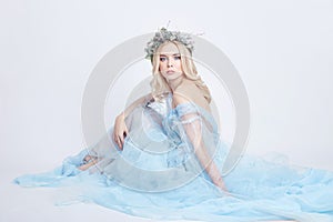 Charming fairy woman in a blue ethereal dress and a wreath on her head on white background, gentle mysterious blonde girl