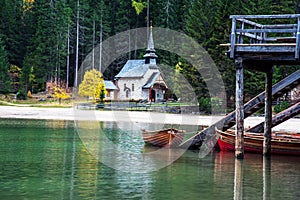 Charming fascinating autumn landscape with a church and boats on the lake on Fanes-Sennes-Braies natural park in the Dolomites in