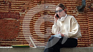 Charming female having conversation on phone while sitting on curb outdoors