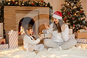 Charming female kid presenting Christmas gift to her mother at Christmas morning, celebrating Christmas and New Year, happy time