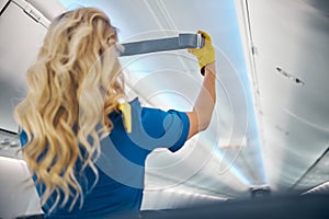 Charming flight attendant in yellow gloves working on the plane with equipments for safety on board