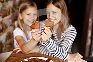 Charming, funny and laughing girls on a blurry background are holding heart-shaped cookies on an outstretched arm, two hearts