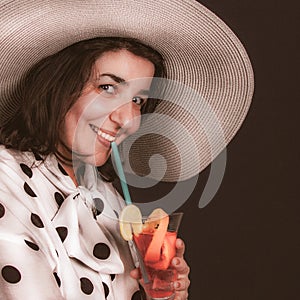 Charming girl drinks cocktail. Happy laughing brunette with a glass of tropical cocktail in her hand. Close-up, retro style