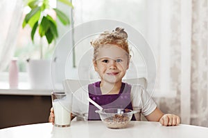 Charming girl eats cereal with milk for Breakfast and . On the table are chocolate flakes, a glass of milk. Healthy