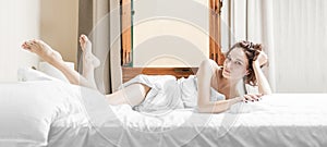 Charming girl lies in bed. She stretched out her legs and looks playfully at the camera. The concept of relaxation, spa, hotels,