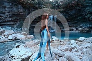 Charming girl with long luxurious healthy black hair posing in front of high waterfall in lagoon with blue clear water