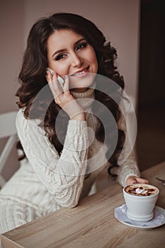 Charming girl with long wavy hair talking over mobile with cup o