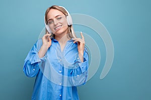 charming girl with pleasure listens to music in big headphones on a blue isolated background