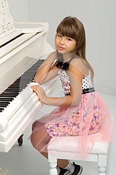 Charming girl sitting at white grand piano