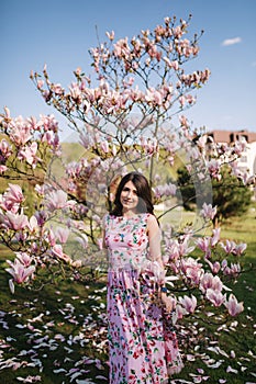 Charming girl stand by the beautiful pink magnolia tree outside. Gorgeous lady