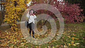 Charming girl walks in colourful autumn park, puts on hat and smiles