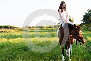 Charming girl in white dress sitting on horse in the field