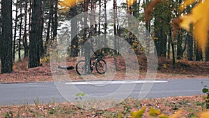 Charming good-looking man in sportswear finished cycling training on road bike at autumn forest and drinking water. Professional m