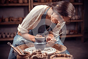Charming handicraftsman creates a new pottery from clay on a potter`s wheel. Pottery workshop.