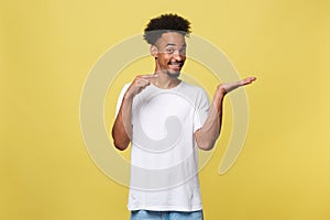 Charming handsome young black man holding his hand up to show present sell product. Isolated over yellow background.