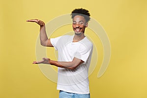 Charming handsome young black man holding his hand up to show present sell product. Isolated over yellow background.