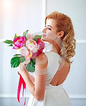 Charming happy and joyful young woman bride in white dress with bouquet of flowers in studio