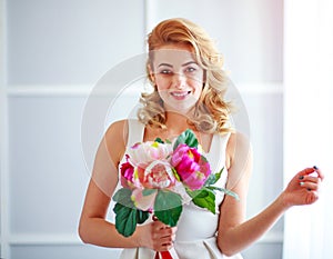 Charming happy and joyful young woman bride in white dress with bouquet of flowers in studio