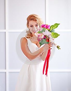 Charming happy and joyful young woman bride in white dress with bouquet of flowers in studio