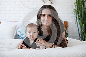 Charming happy little baby boy having fun with mom brunette woman on bed in the bright bedroom