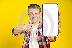 Charming happy man pointing at smartphone with white empty screen, wearing red plaid shirt and jeans cellphone display