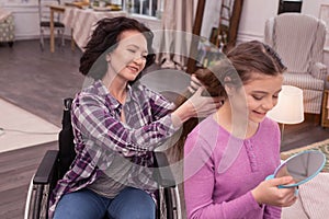 Charming immobile woman helping girl with hairstyle