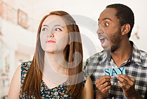 Charming interracial couple holding up small letters spelling the say while interacting happily, blurry studio