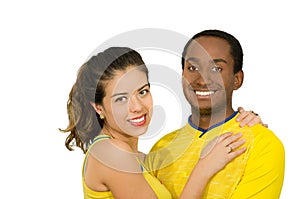 Charming interracial couple wearing yellow football shirts, embracing friendly while posing for camera, white studio