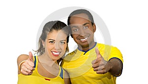 Charming interracial couple wearing yellow football shirts giving thumbs up to camera, white studio background