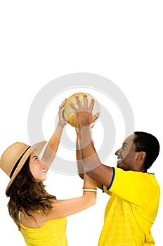 Charming interracial couple wearing yellow football shirts holding ball up in air between each other, profile angle