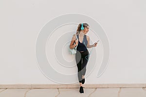 Charming joyful young woman in sportswear enjoying chatting on phone, lovely music in headphones on white background