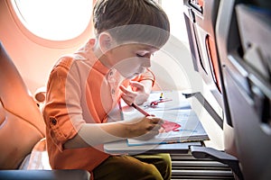 Charming kid traveling by an airplane. Joyful little boy sitting by aircraft window during the flight. Air travel with little kids