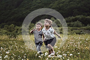Charming kids on walk in clearing relax among wild beautiful flowers. Happy childhood in nature. Children brother and sister run
