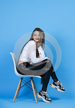 Charming lady in white shirt, posing with head on hand, while sitting on chair with crossed legs.