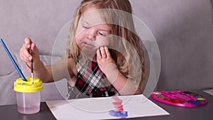 Charming little blonde girl in red checkered dress, painting with colorful paints. childhood, art, paint