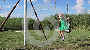 A charming little blonde girl is swinging at a green field.