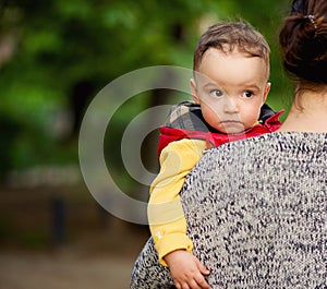 A charming little boy looks over his mother`s shoulder.