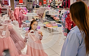 Charming little girl choosing elegant dress at shopping mall