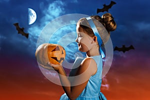 Charming little girl in a costume of the Cinderella princess holds a pumpkin on the background of the