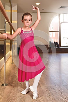 Charming little girl dreams of becoming a ballerina. The girl in the pink dress is dancing, holding on to the bar.Baby girl is