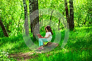 Charming little girl in forest with book sitting on tree stump