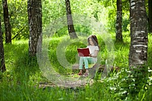 Charming little girl in forest with book sitting on tree stump