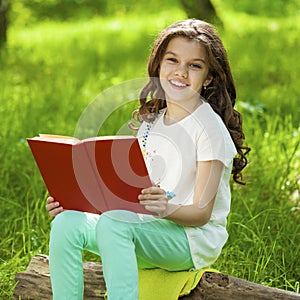 Charming little girl in forest with book sitting on tree stump