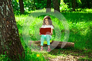 Charming little girl in forest with book sitting on tree stump