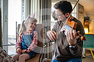 Charming little girl learning to play the violin with an artistic music teacher.