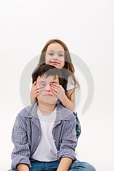 Charming little girl - loving sister hugging her brother - a teenage boy - from the back, isolated over white background