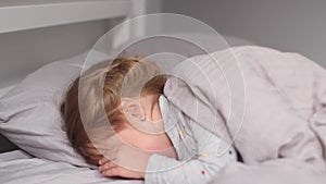 Charming little girl lying on bed in gray bedroom. Morning routine, childhood, daughter. Full hd footage