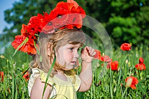 Charming little girl in a poppy field with a bouquet of poppies on her head